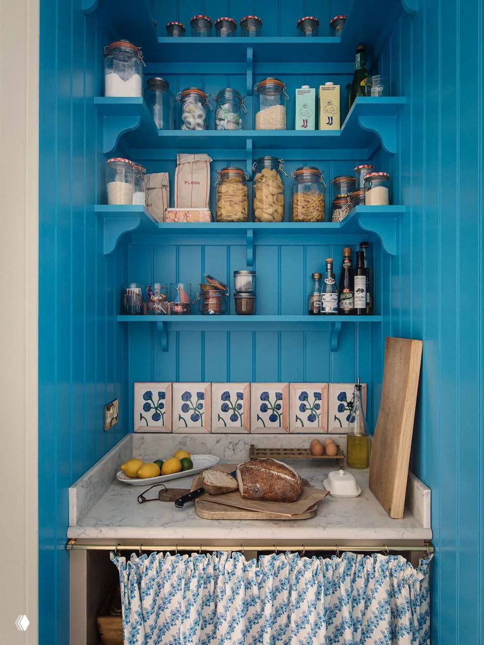 Глубокая узкая ниша, выкрашенная в насыщенный бирюзовый цвет, с открытыми полками и маркёрованными банками — яркая компактная кладовая в ограниченном пространстве.