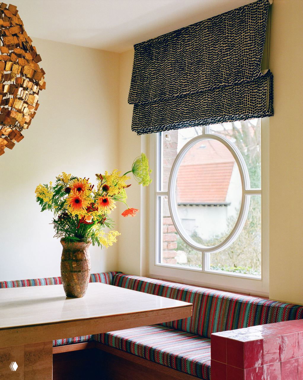 Спальня с белым покрывалом и декоративным оранжево-кремовым узором на обоях, камин окрашен в тёплый коралловый оттенок, деревянные полки для книг вокруг.