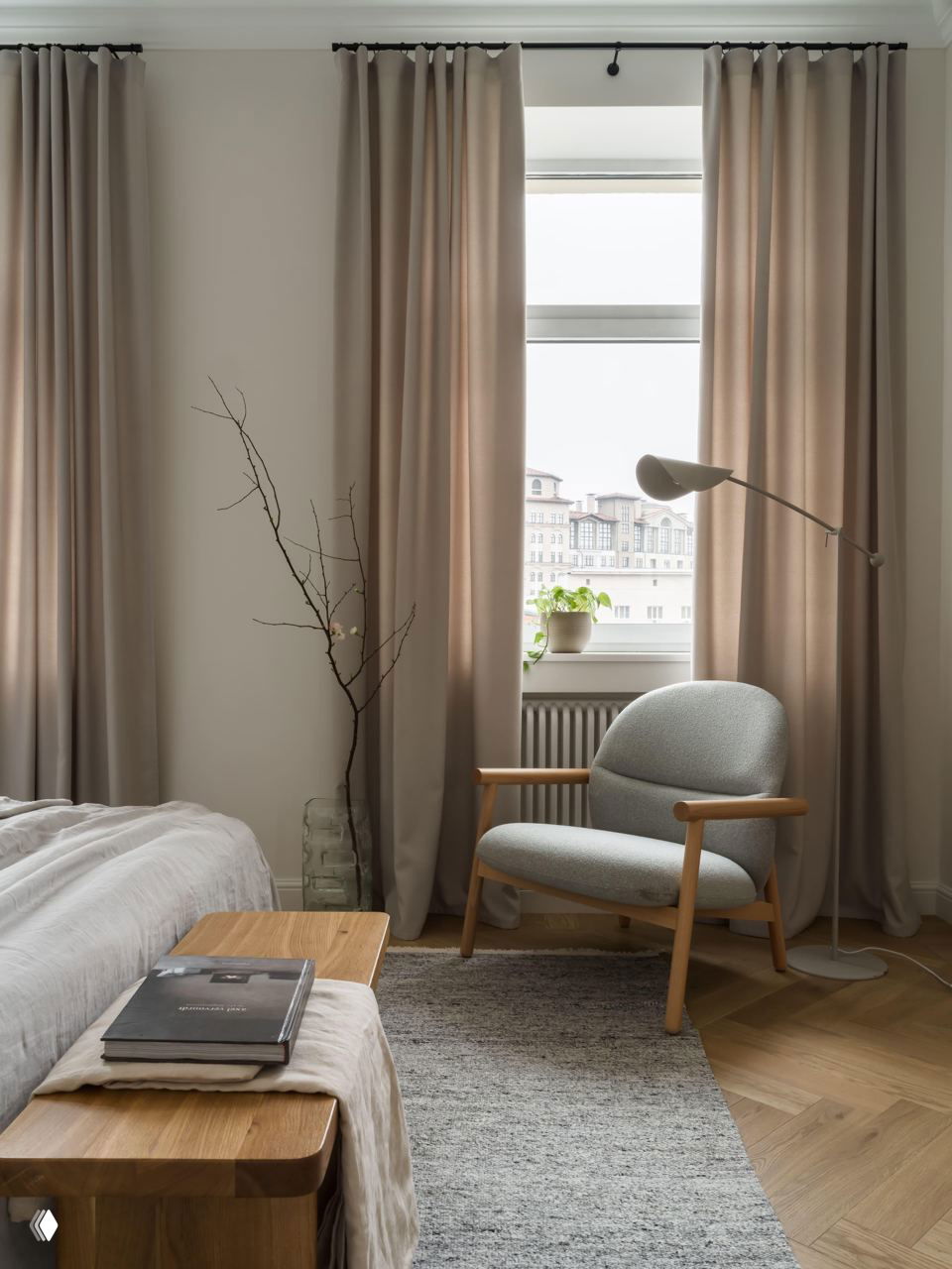 Спальня с большим окном и портьерами, уютное кресло с деревянными подлокотниками, простой текстиль и низкая скамья у изножья кровати, естественная гамма.