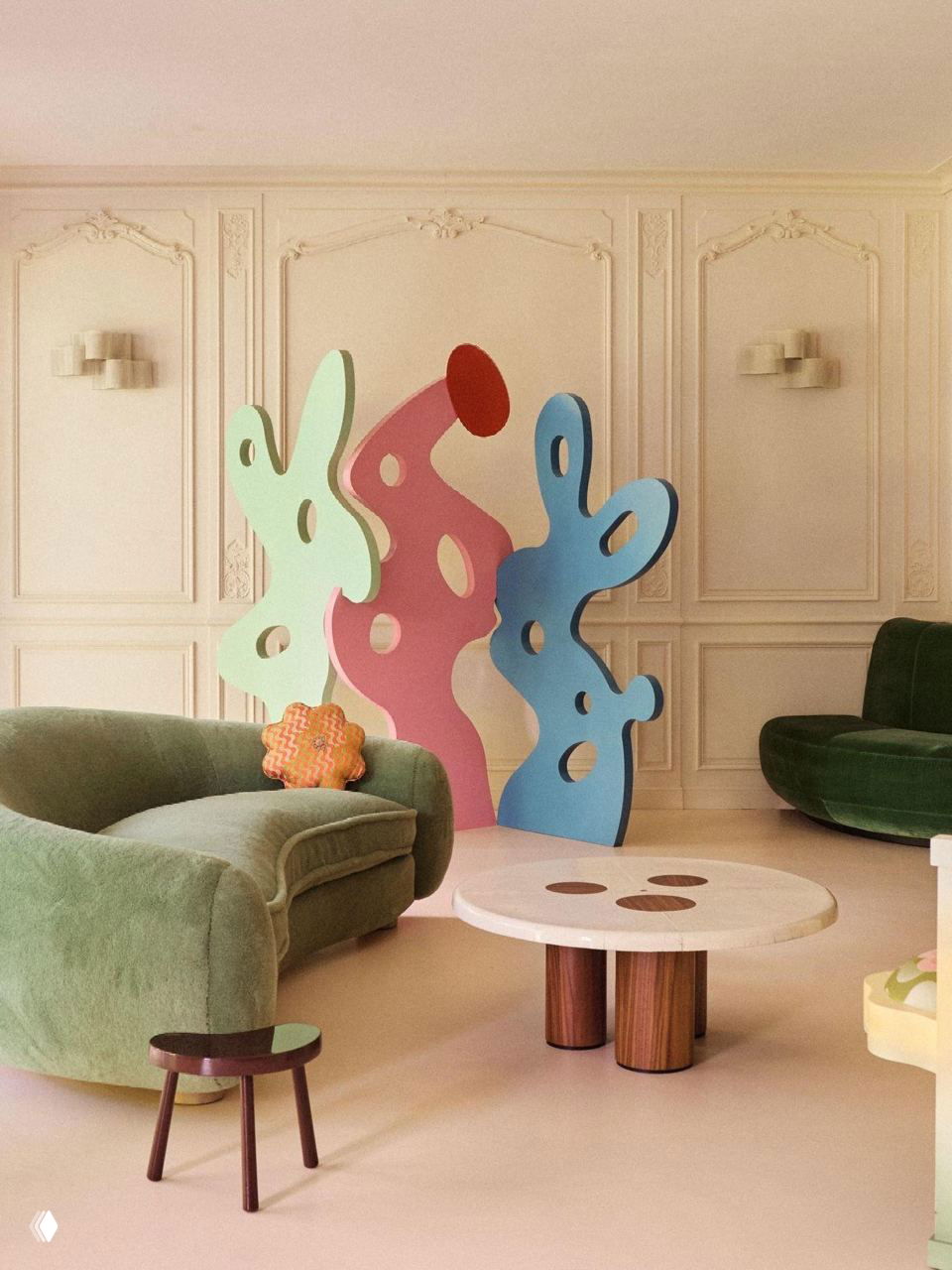 Гостиная в пастельных тонах: зелёные бархатные диваны, цветные абстрактные перегородки‑скульптуры, круглый кофейный стол и мягкое освещение.