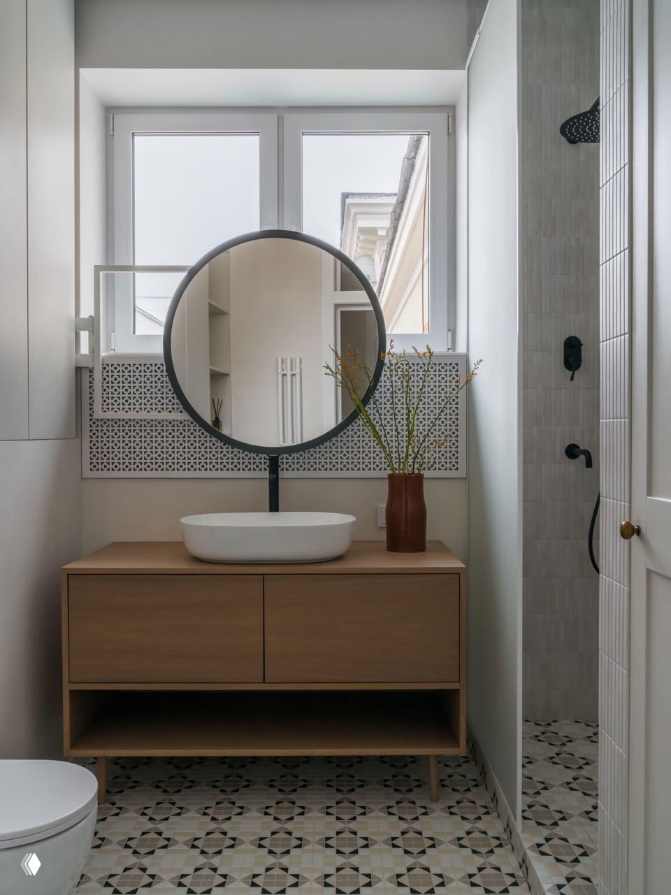 Ванная комната: круглая зеркальная композиция над деревянной тумбой с накладной раковиной и декоративной вазой, мраморная или керамическая плитка на полу с узором.