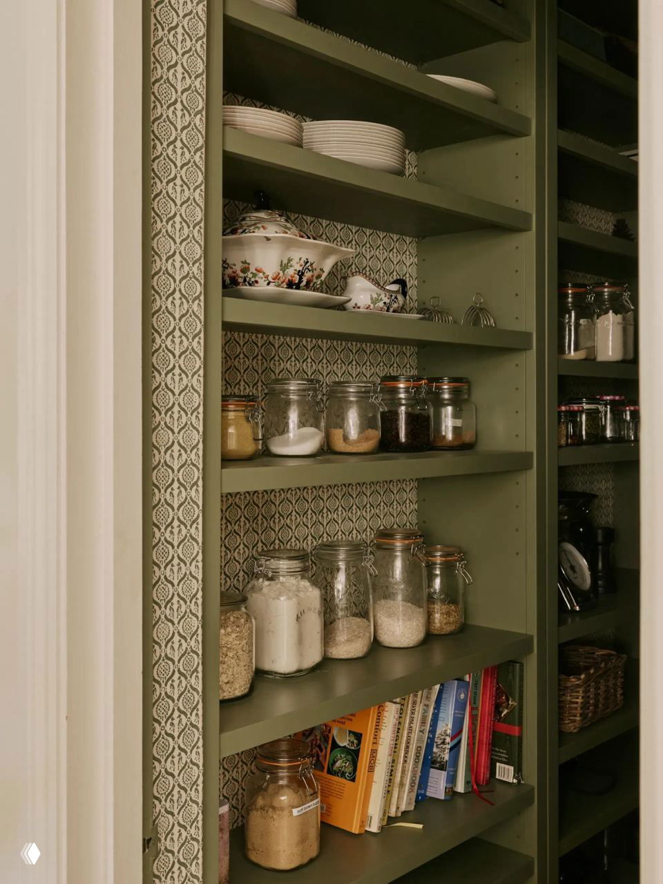Узкая встроенная кладовая с зелёными полками и аккуратно расставленными банками, книгами и мелочами — пример рационального использования глубокой ниши.