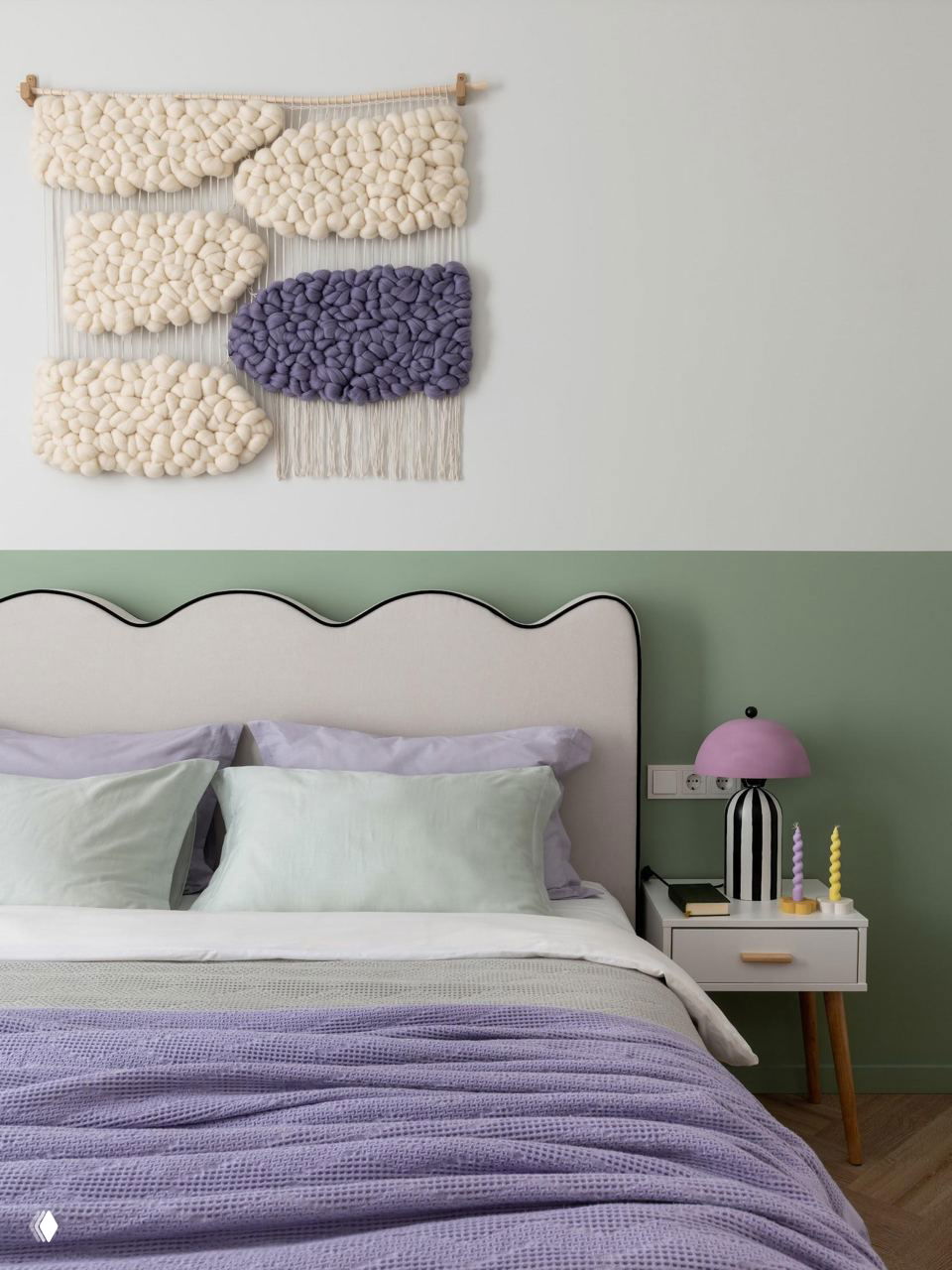 Спальня с мягким изголовьем, настенным текстильным панно в технике тафтинг, зелёная нижняя часть стены и фиолетовый плед крупной вязки на кровати.