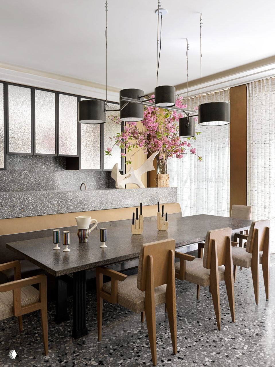 Столовая с темной каменной столешницей, ансамблем подвесных светильников и столом на фоне крупного окна и штор.