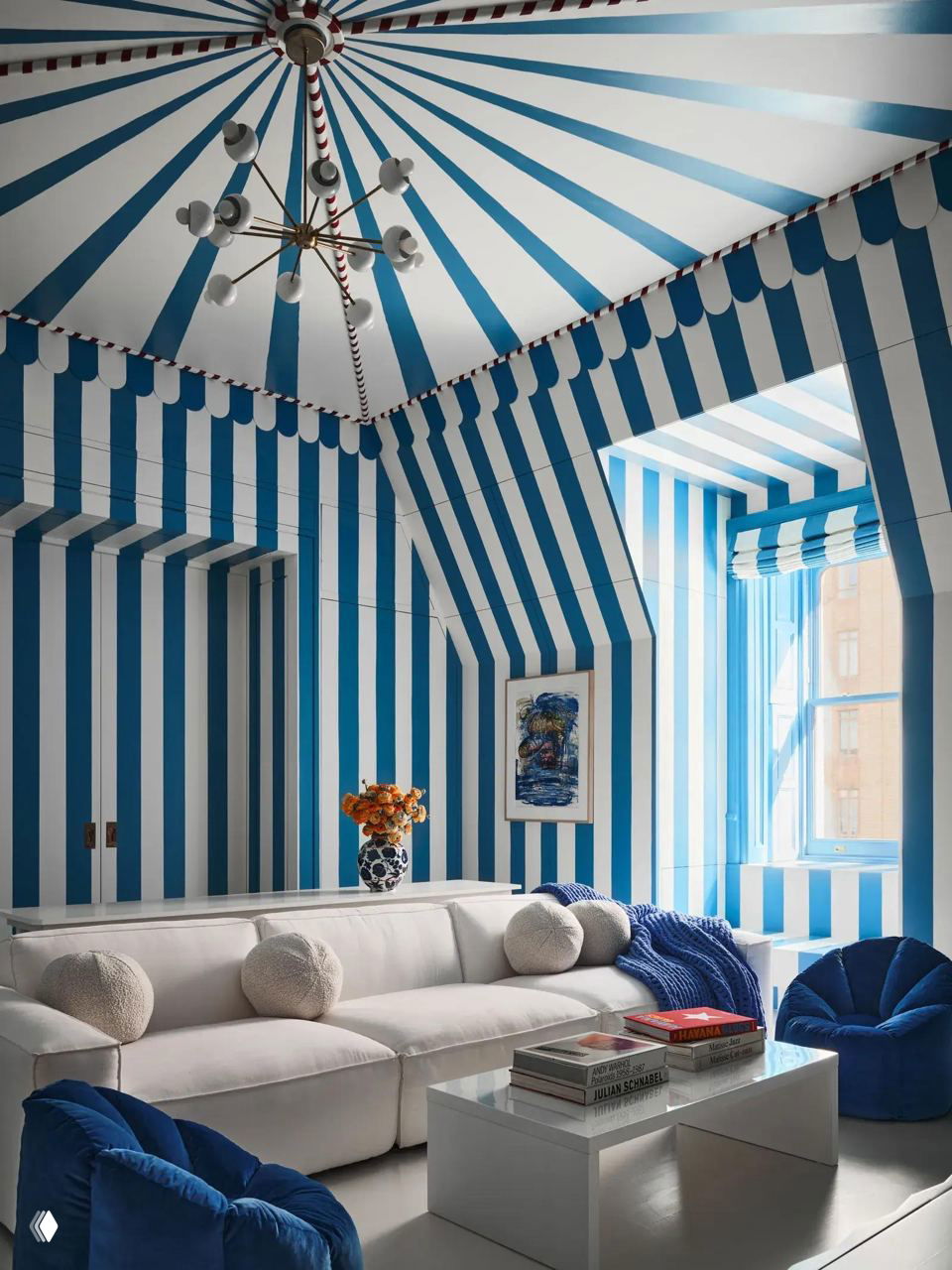 Комната с сине‑белыми полосами на стенах и потолке в форме купола, белый диван, синие мягкие кресла и небольшие столики создают эффект цирковой графики.