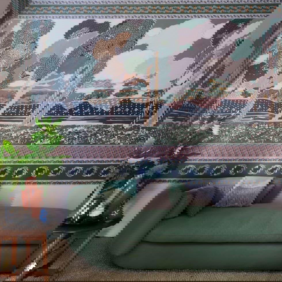 Стена с крупным узором и растительными мотивами в спокойной природной палитре: обои‑панно с горизонтальными бордюрами и зелёным диваном на переднем плане.