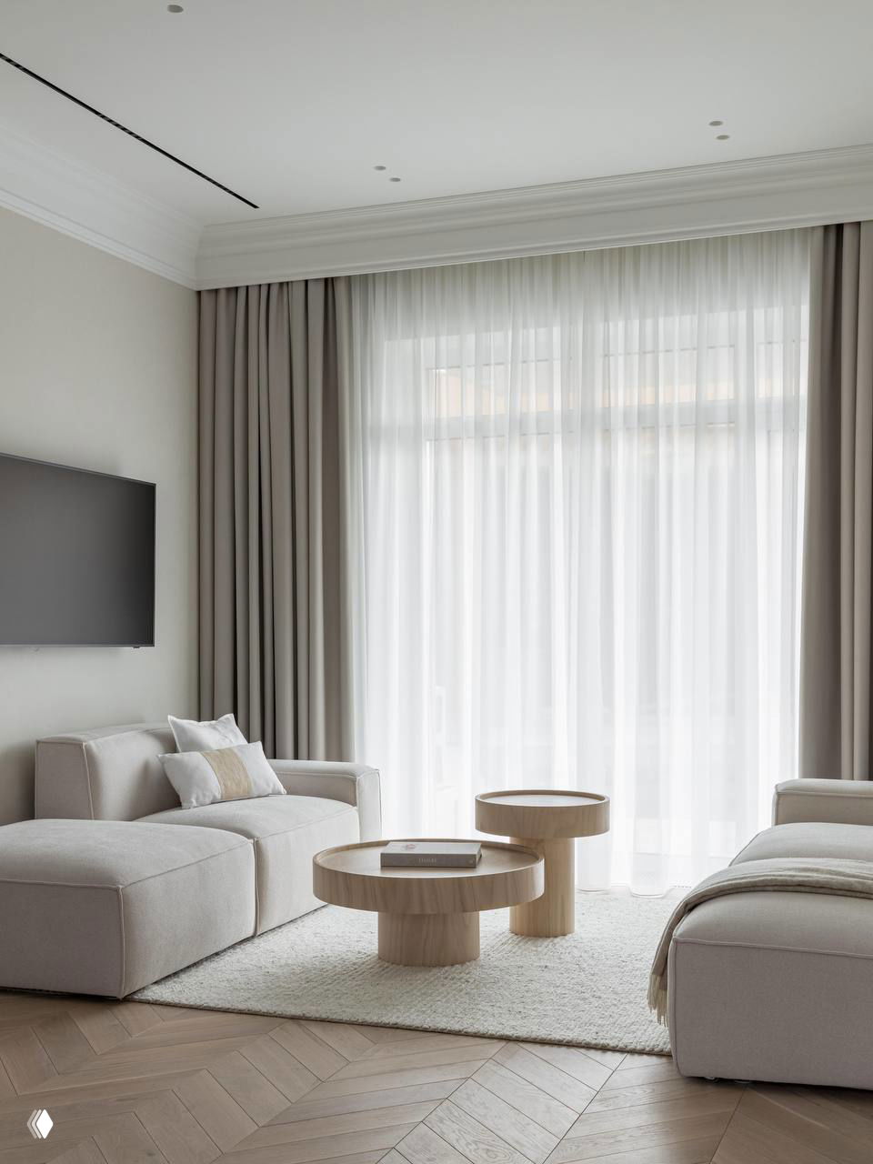 Светлая гостиная таунхауса с мягкими светло-бежевыми диванами, круглыми низкими деревянными столиками и крупными шторами, уютное оформление.