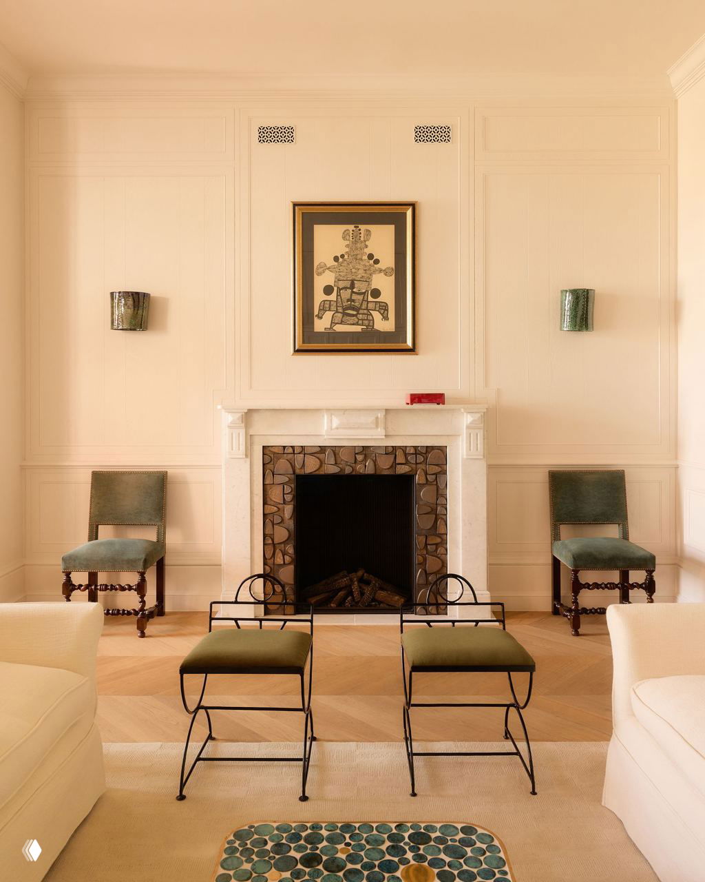 Комната с камином: белая мраморная каминная полка, рисунок над камином, две стулья и металлические подставки для ног на паркетном полу в мягком свете.