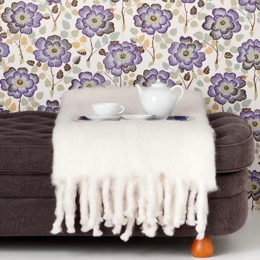 Крупный план уютного кресла и пушистого пледа на фоне цветочных обоев — пример декоративной текстуры и мягкого скандинавского акцента в интерьере.