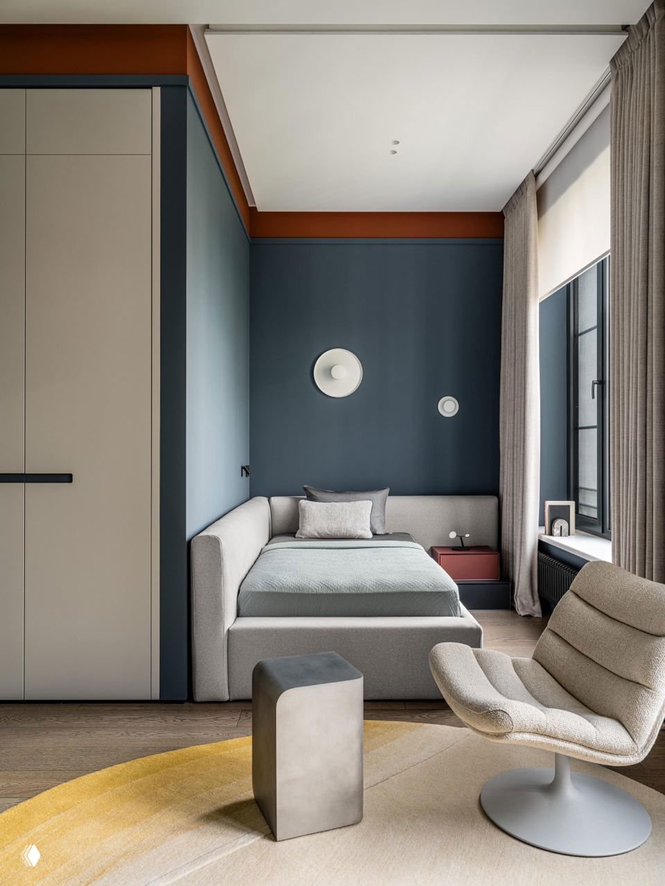 Спальня‑ниша с мягкой кроватью в светлой обивке, круглый ковер и кресло‑поворот в спокойной нейтральной палитре с синими акцентами.
