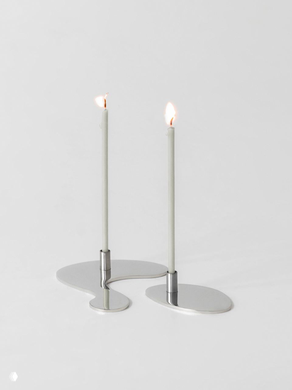 Нержавеющий металлический подсвечник в форме плавной лужи с двумя высокими тонкими свечами и минималистичной белой подложкой — предмет из линии objects.dpt бюро .dpt.