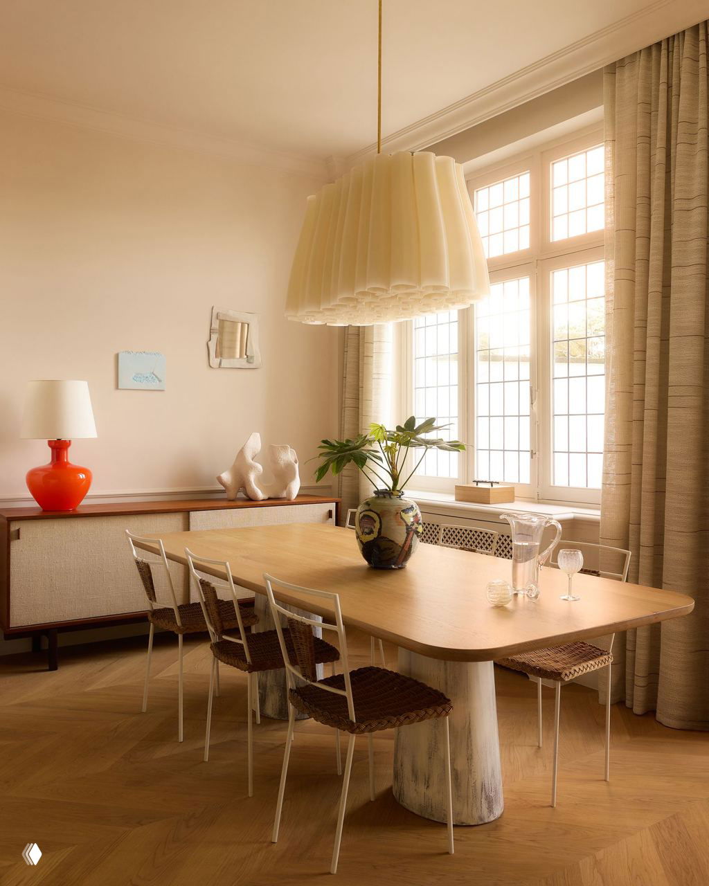 Столовая с большим деревянным столом, подвесной лампой и стульями с плетёными сиденьями — сочетание классических форм и современного декора на тёплом паркете.