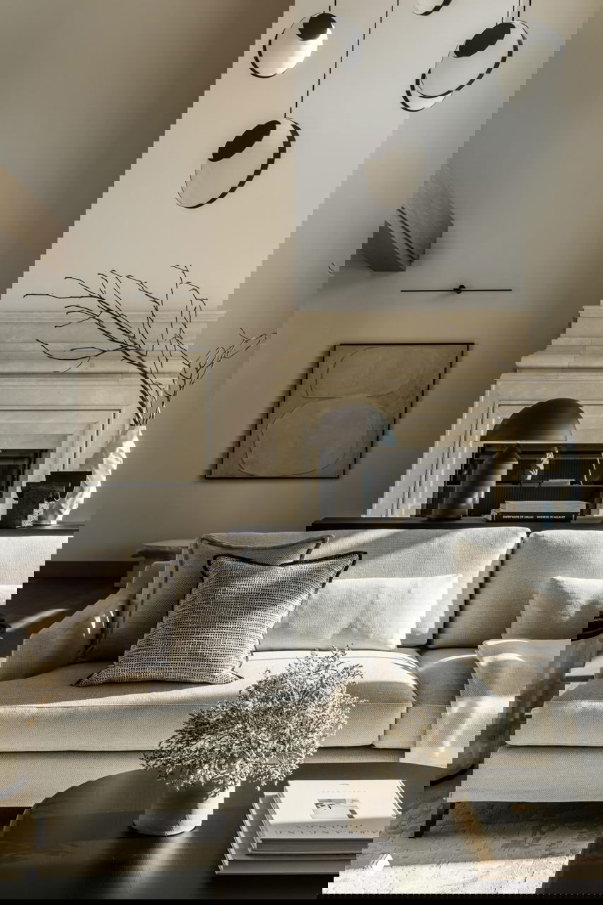 Уютная зона с кремовым диваном у камина и декоративными предметами, текстуры тканей и скульптурные светильники подчёркивают эклектичный минимализм.