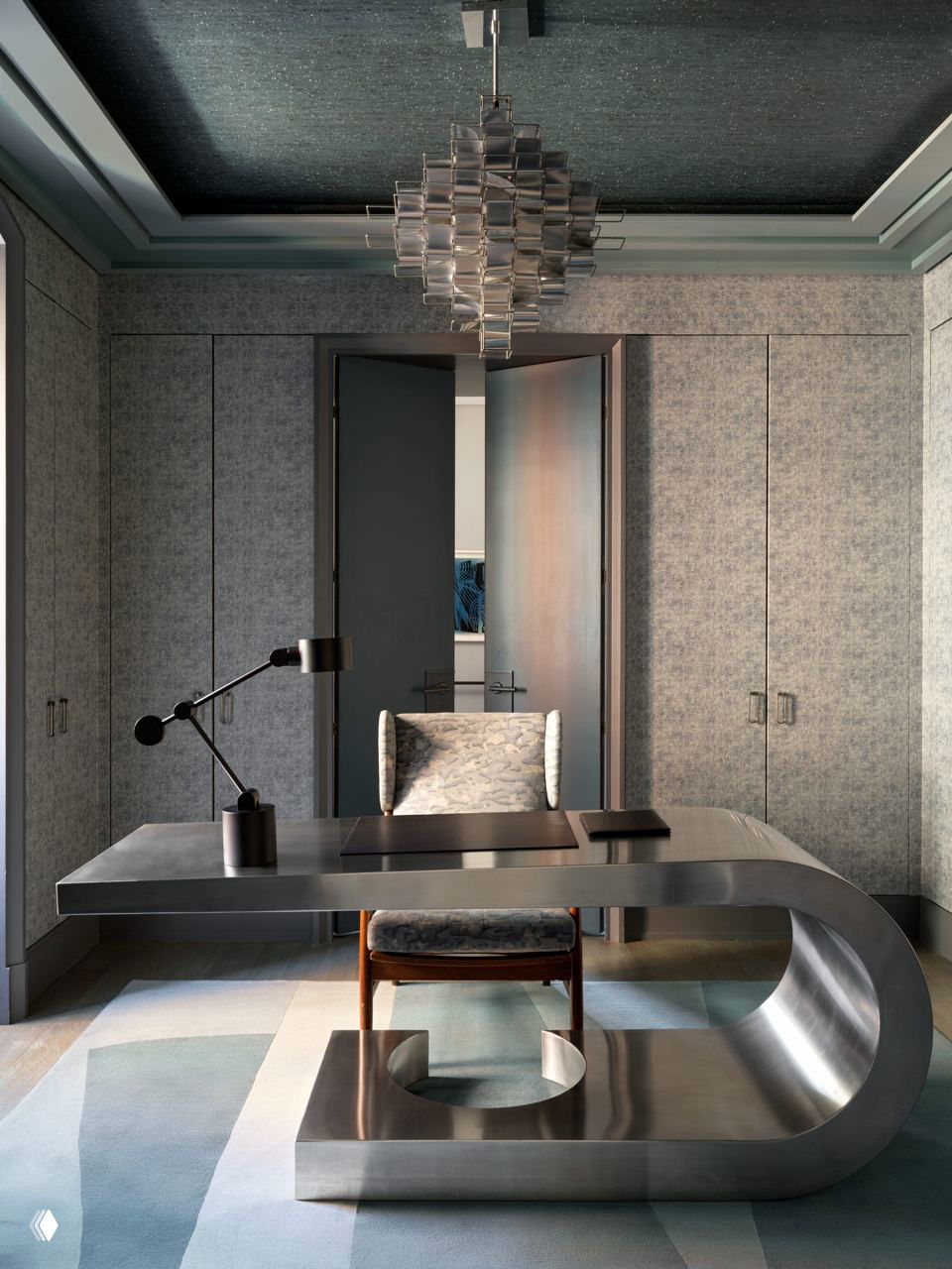 Кабинет с выразительным металлическим столом в форме 'С', мягким креслом и приглушенным освещением — элегантный рабочий интерьер.