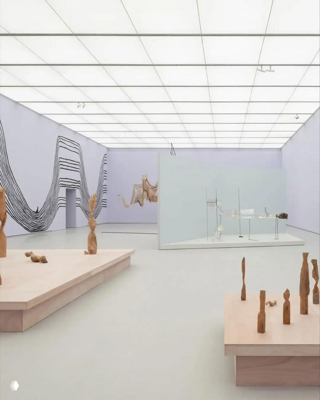 Выставочный зал с подиумами и скульптурами на нейтральном фоне, ровным потолочным светом и графическими элементами на стенах интерьера.