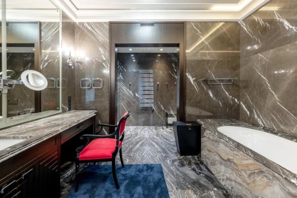 Ванная комната с тёмным мраморным оформлением: большая ванна, столешница с зеркалом, кресло и хромированные аксессуары на фоне стен из камня.