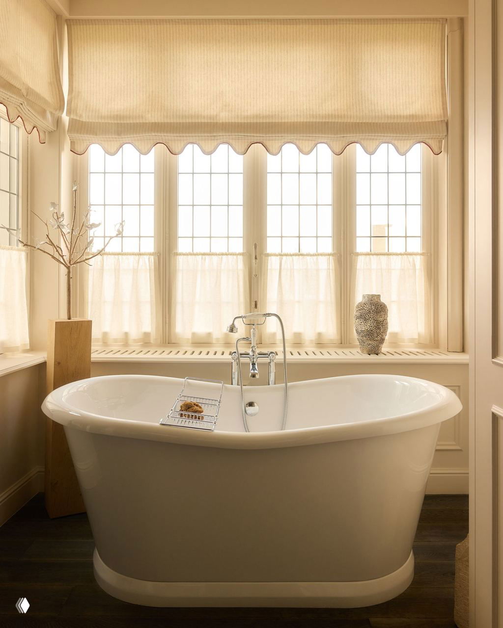 Уютная ванна на ножках у большого окна с жалюзи и лёгкими шторами, на подоконнике стоит декоративная ваза — интерьер, залитый естественным светом.