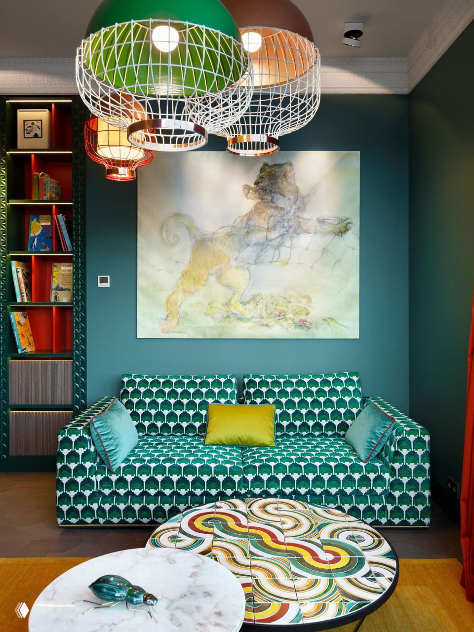 Яркая комната с зелёным узорчатым диваном, крупной живописной картиной на тёмно-зелёной стене и разноцветными подвесными светильниками.