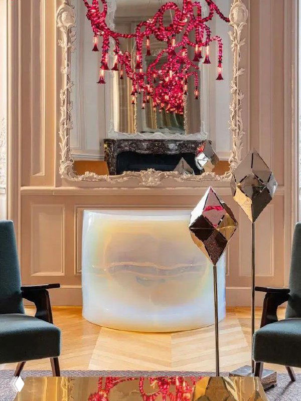 Отражающие геометрические скульптуры на стойках, перламутровая консоль и яркая розовая люстра в декоративной комнате Hôtel de Maisons — инсталляция на ярмарке.