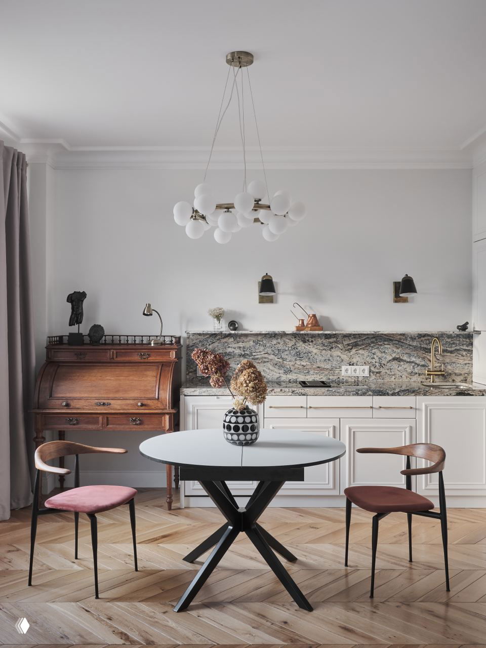 Светлая кухня без верхних шкафов с круглым столом, висячей люстрой и мраморной фартукой — интерьер с паркетом и винтажным секретером рядом.