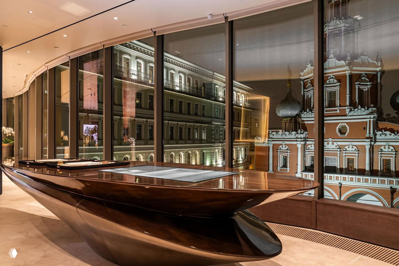 Интерьер резиденции MR Private: массивный стол в форме яхты на фоне панорамного окна с видом на исторические фасады Москвы.