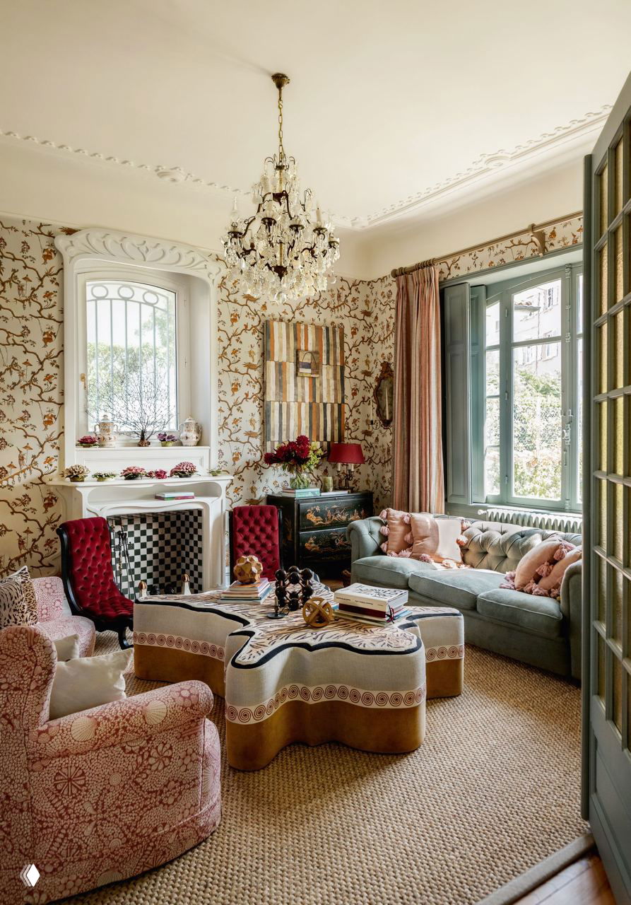 Гостиная с богатым узорчатым обоям, хрустальной люстрой и разноцветной мягкой мебелью — эклектичный интерьер с винтажными деталями.
