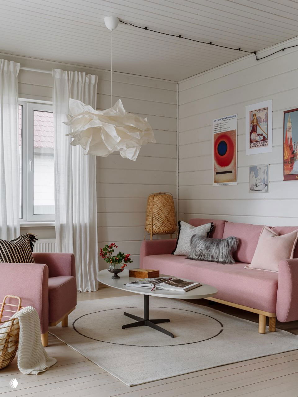 Гостиная с белыми деревянными панелями, розовым диваном и креслом, круглым столом и мягким ковром, уютная композиция интерьера дачи.