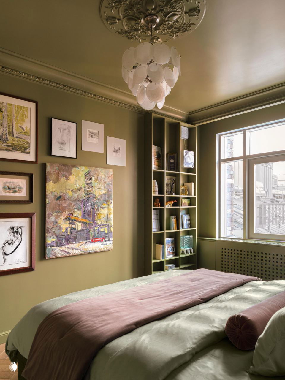 Угол спальни с художественной стеной: картины и открытая ниша-стеллаж с книгами и аксессуарами на фоне зелёных стен.