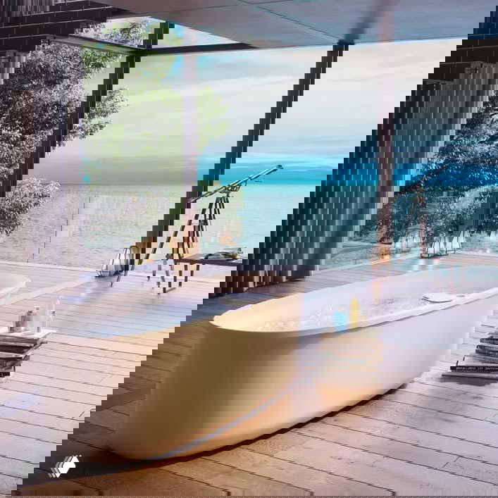 Овальная ванна на открытой террасе с видом на море и аксессуарами — показательное решение для уютной зоны отдыха в интерьере ванной комнаты.