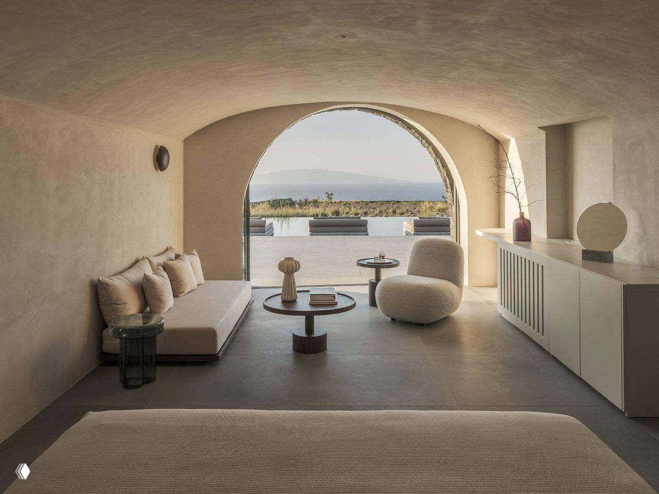 Гостиная с арочным проходом к наружной террасе: натуральные нейтральные оттенки, низкая мебель и вид на открытое пространство и море.