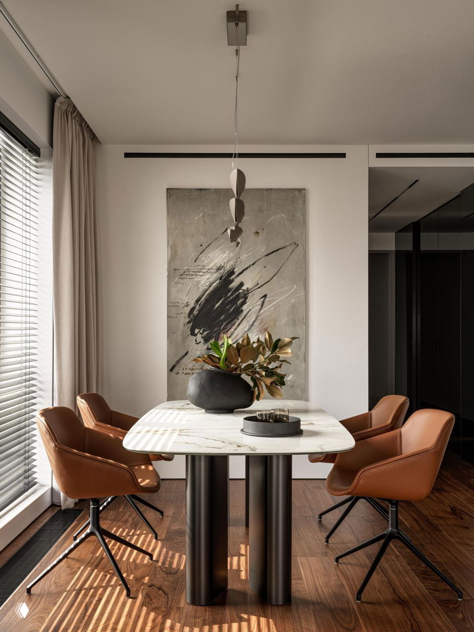 Обеденная зона с мраморным столом на массивных цилиндрических опорах, четырьмя коричневыми кожаными креслами и вазой с зеленью у панорамного окна.