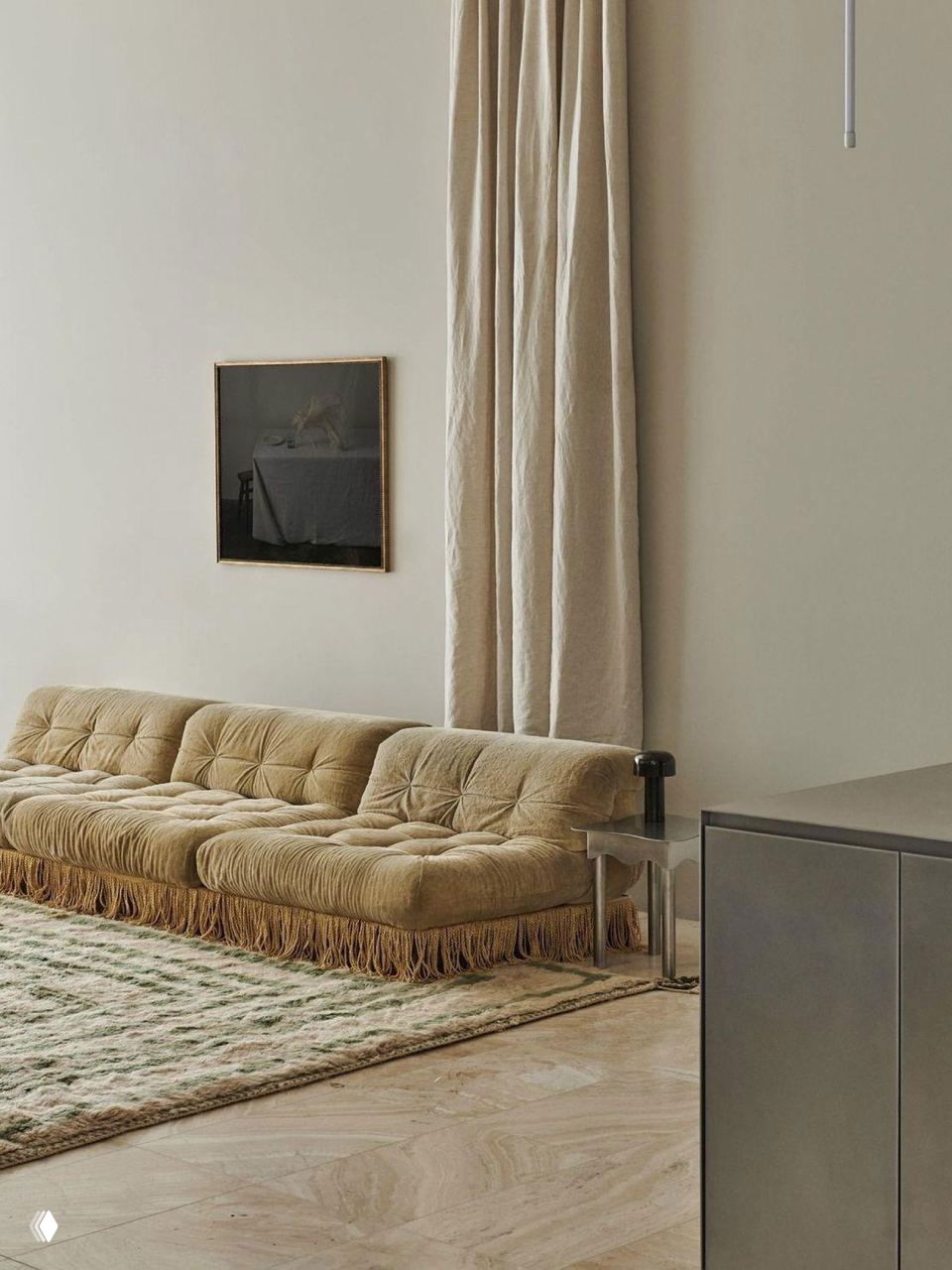 Низкий велюровый диван нейтрального тона с богатой бахромой и мягким ковром — очевидная отсылка к мебельным формам 1980‑х в интерьере.