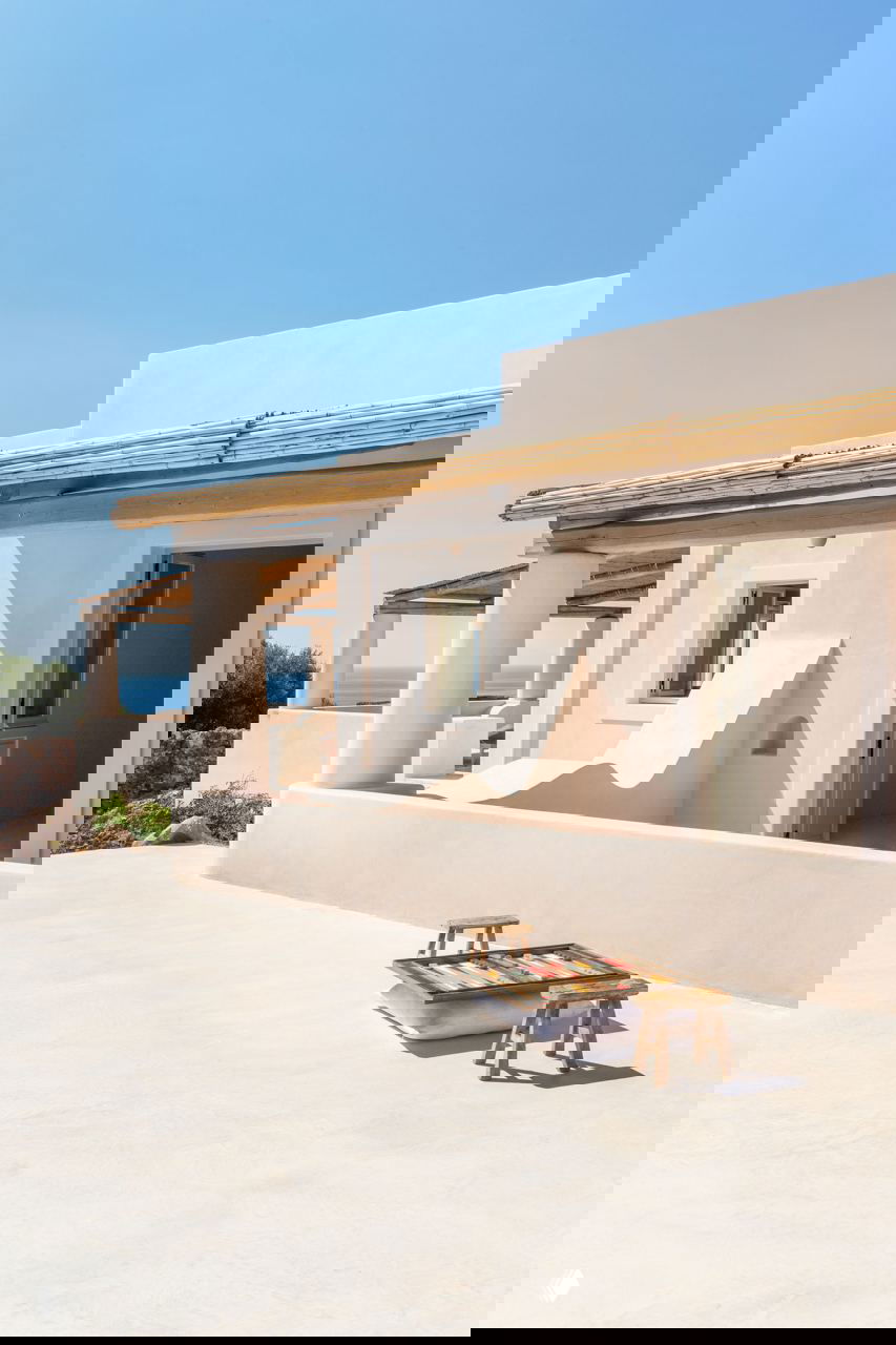 Терраса минималистичного дома на Филикуди с ровной светлой площадкой, деревянным навесом, низкой мебелью и видом на море и небо.