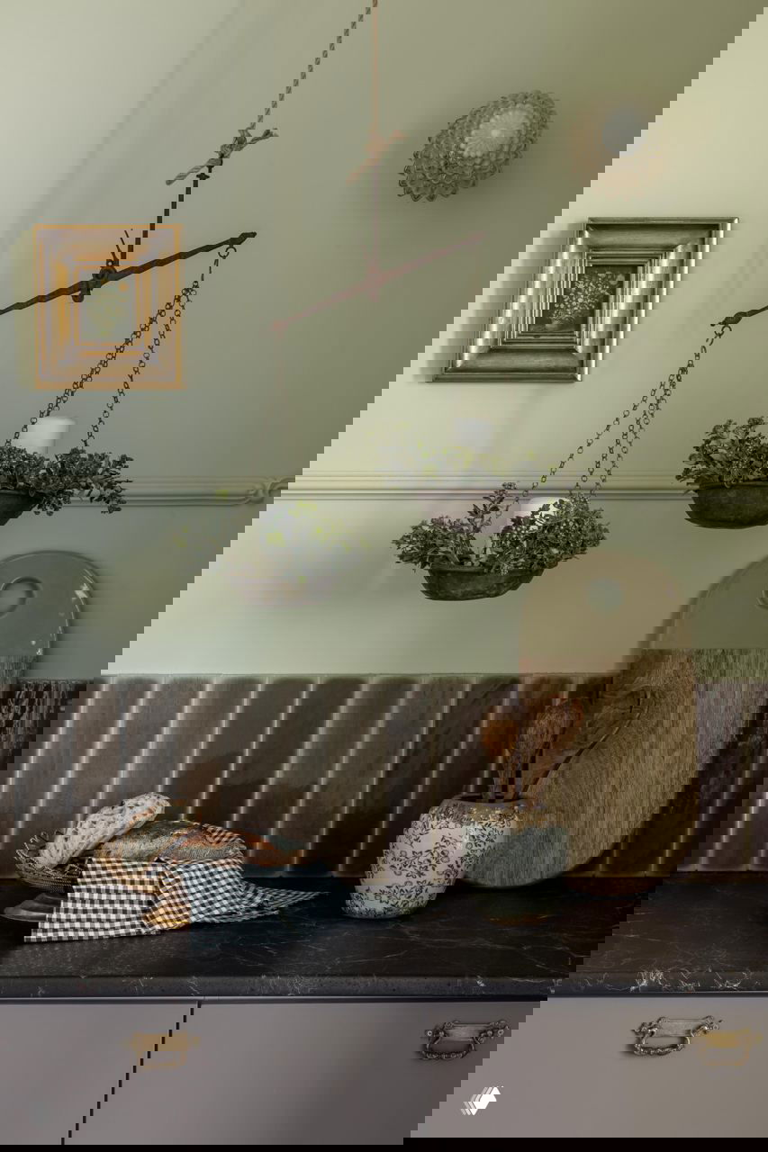 Кухонная композиция с висящими чугунными чашами-кашпо, хлебом на каменной столешнице и разделочными досками на фоне зелёной стеновой панели.