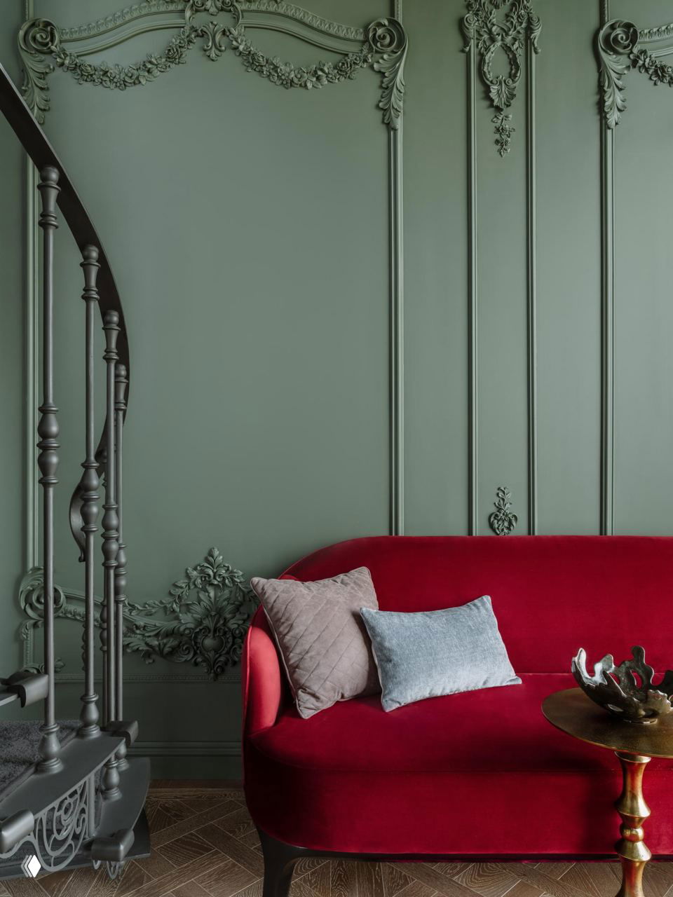 Классическая стена с лепниной в оливково‑зелёном цвете и насыщенно‑красный бархатный диван — сочетание текстур и благородных оттенков.