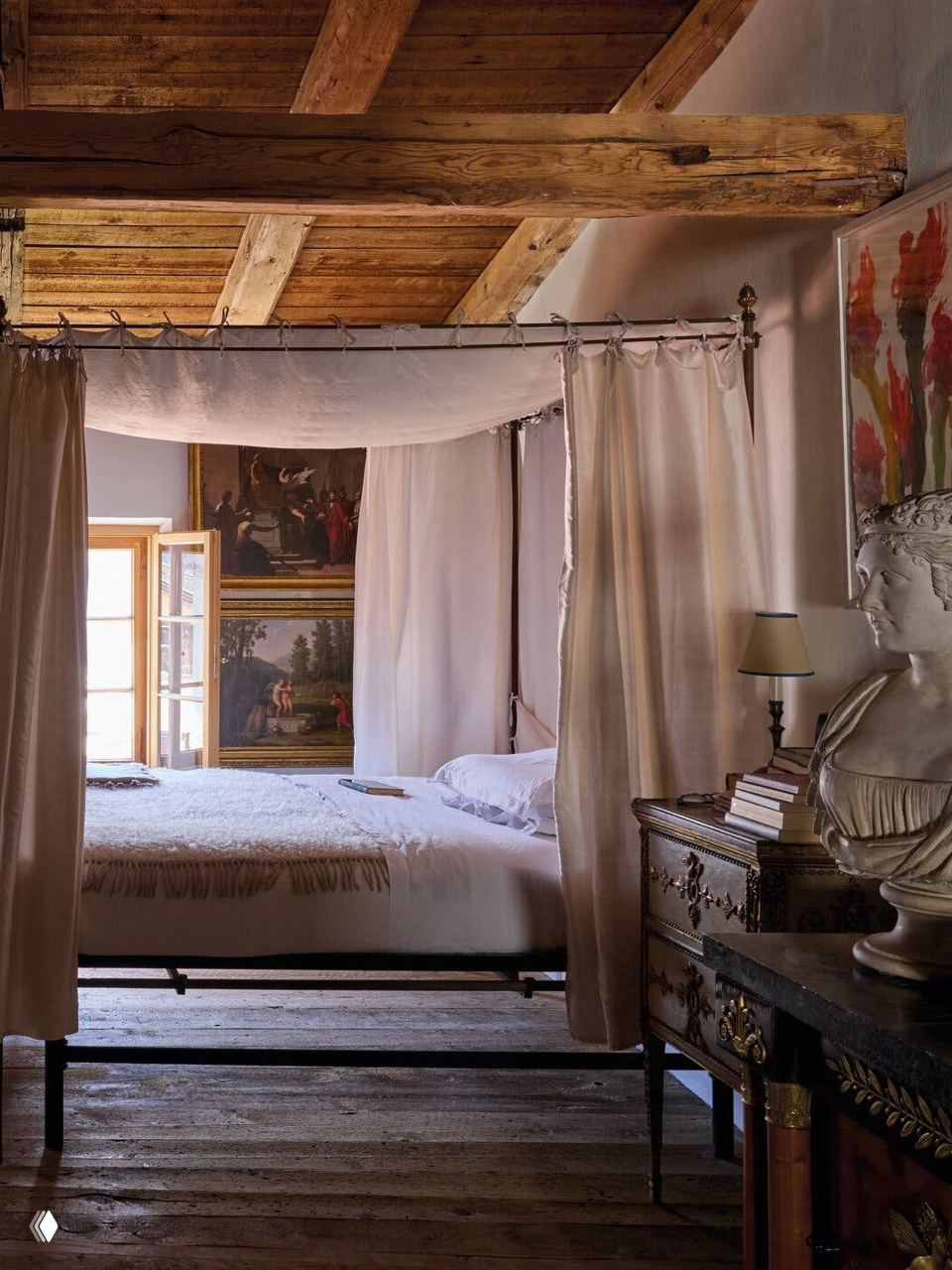 Спальня коллекционера с лёгким балдахином, деревянными балками, антикварной тумбой и классическим бюстом у кровати — атмосферный уголок в поместье Спероне.