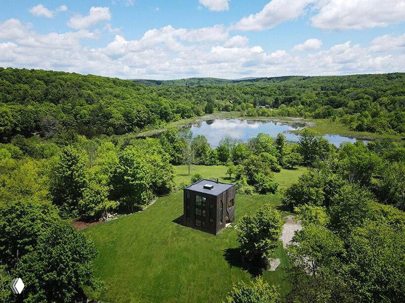 Панорамный вид с холма на лесистый участок и небольшое озеро в долине — место расположения коттеджа FORMA, кадр содержит цифровые артефакты.