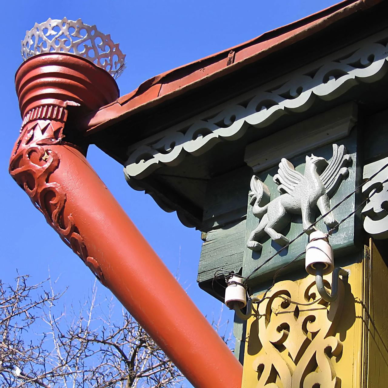Крупный план резной водосточной трубы и декоративного деревянного орнамента фасада традиционного русского дома под ярким небом.