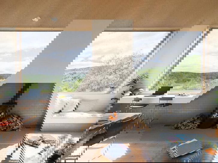 Светлая гостиная с камином, большими окнами и видом на горы Катскилл; интерьер оформлен в теплых древесных тонах и минимализме.