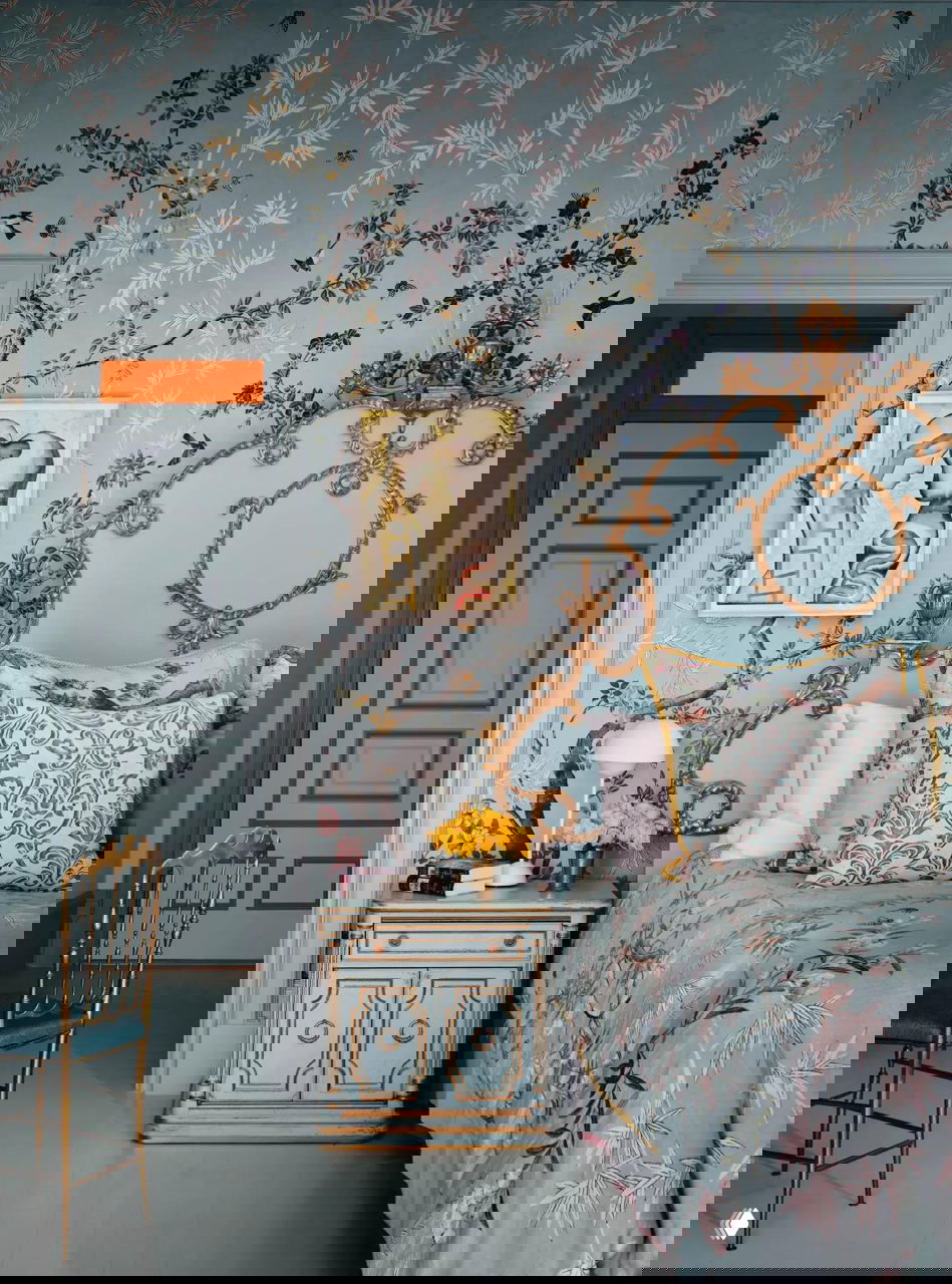 Спальня или кабинет с голубыми стенами, резным золотым изголовьем, цветочными текстилями и декоративной настенной живописью.