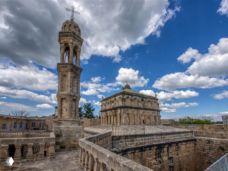Каменная колокольня и церковное здание в Анытлы на фоне выразительного неба: архитектурные детали и крест на шпиле хорошо видны.
