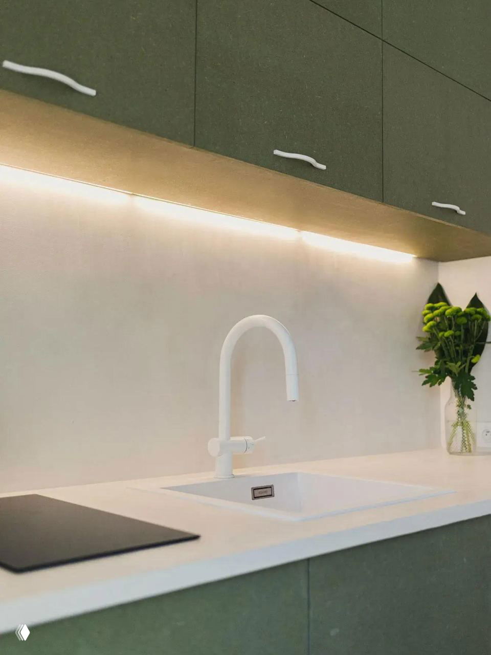 Мини-кухня в мансарде: белая мойка, светлая столешница и зелёные фасады навесных шкафов с подсветкой рабочей зоны.