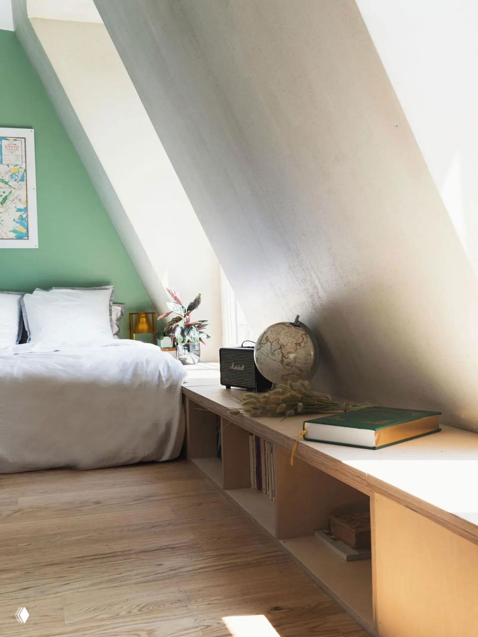 Спальная зона в мансарде: низкая кровать у наклонной стены и длинная скамья-система хранения вдоль окна с книгами и глобусом.