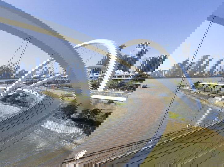 Изогнутая пешеходная трасса моста с поручнями и покрытием для велосипедов, арки создают визуальную цельную ткань над рекой.