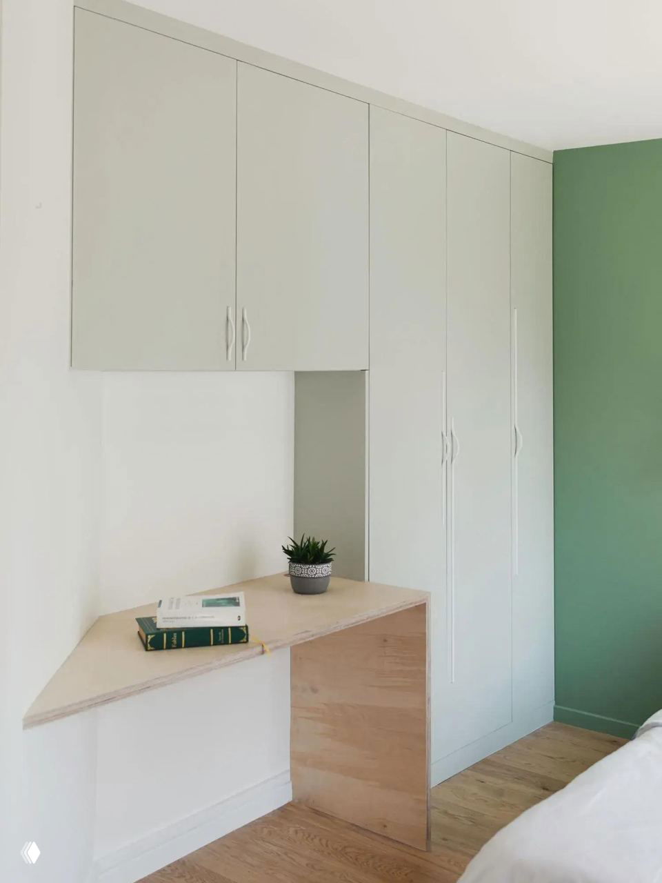 Рабочая зона и встроенные шкафы в мансарде: деревянный стол-подоконник, книги и компактный декор на фоне светлых фасадов.