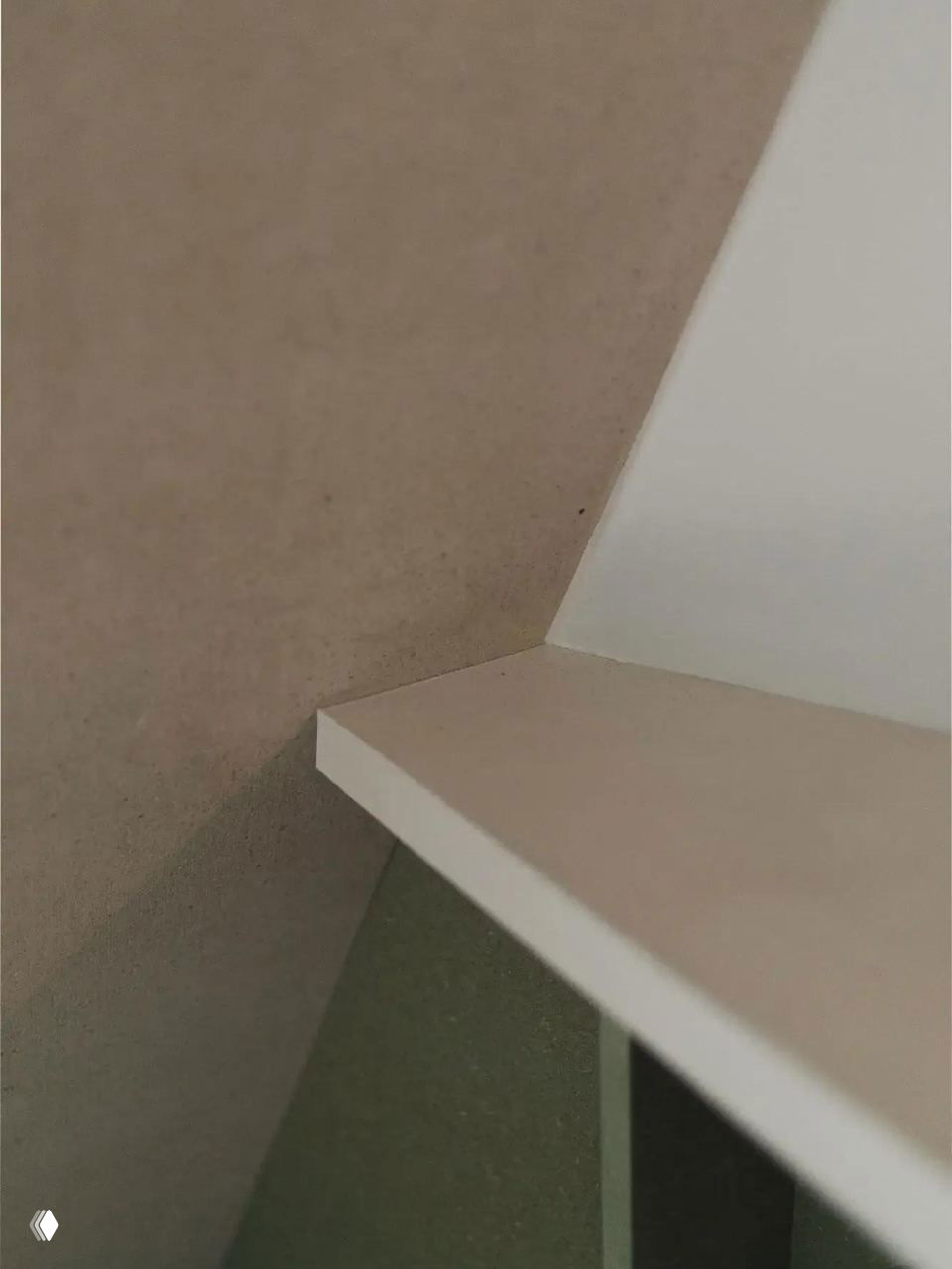 Крупный план архитектурного стыка наклонной стены и полки в мансарде — отделка в пастельных тонах и минималистичный дизайн.