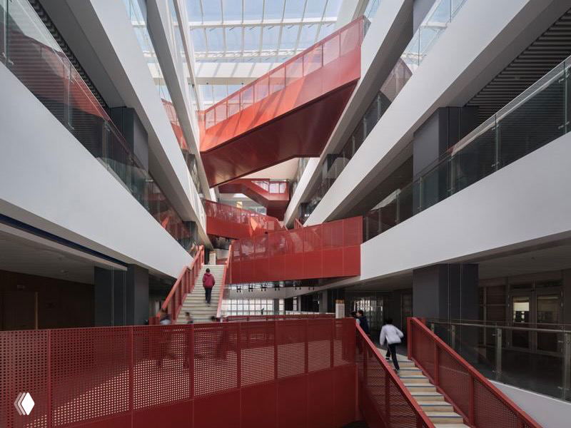 Интерьер главного здания с просторным атриумом: яркие красные лестницы и галереи, обеспечивающие визуальную связь и естественное освещение сверху.
