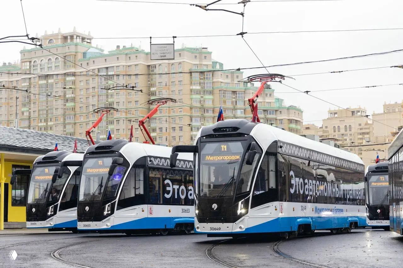 Несколько современных трамваев «Львенок‑Москва» маршрута Т1 на рельсовом кольце в Москве: спереди табло «Метрогородок», на фоне высотные дома и облачное небо.