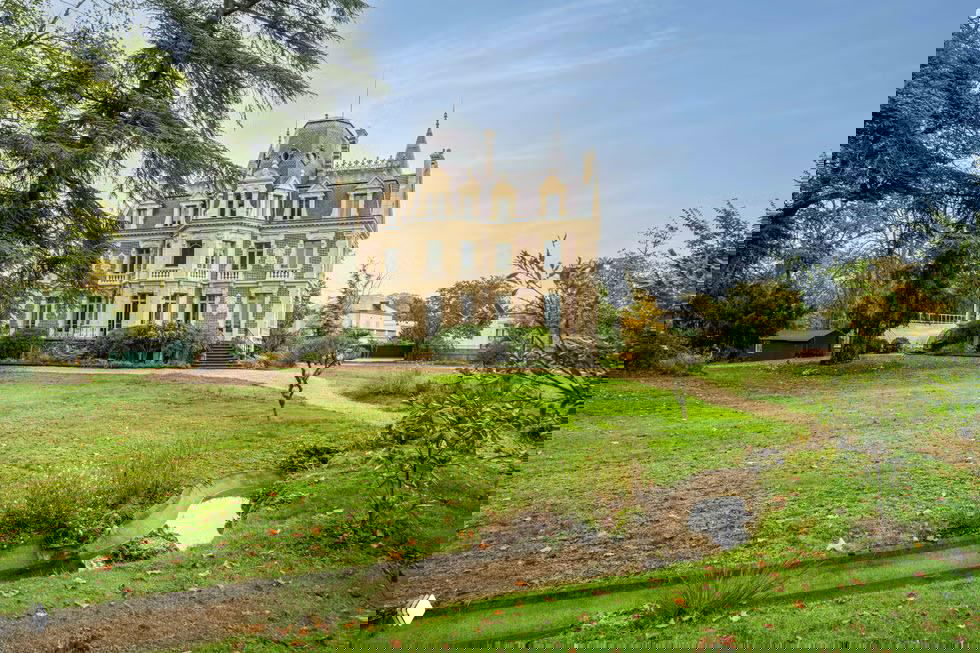 Общий вид особняка Жозефины Бейкер с парком: многослойная кровля с башенками, крупный зеленый газон и древесные насаждения вокруг исторической постройки.