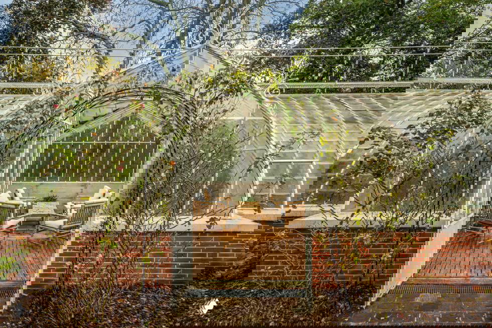 Английская оранжерея и вход в теплицу на территории особняка: стеклянные панно, кирпичная низкая стенка и уютная лаундж-зона внутри.